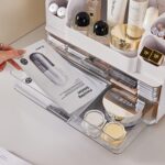 Heaime white acrylic makeup organizer with two drawers and an open top section holding brushes, lipsticks, and skincare bottl
