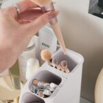 Heaime white acrylic makeup organizer with two drawers and an open top section holding brushes, lipsticks, and skincare bottl