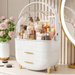 A white and gold NestOrganix makeup organizer with three drawers and a clear top cover, filled with various cosmetics.