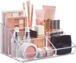 Clear plastic vanity makeup organizer with six compartments, holding various beauty brushes and cosmetic items.