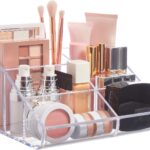 Clear plastic vanity makeup organizer with six compartments, holding various beauty brushes and cosmetic items.