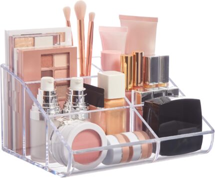 Clear plastic vanity makeup organizer with six compartments, holding various beauty brushes and cosmetic items.