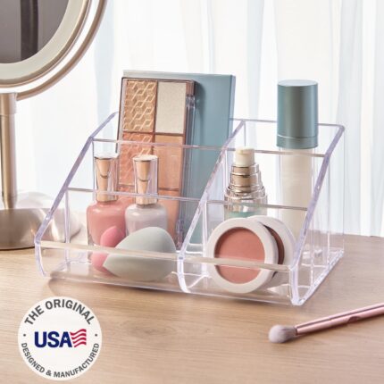 Clear plastic vanity makeup organizer with six compartments, holding various beauty brushes and cosmetic items.
