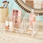 Clear plastic vanity makeup organizer with six compartments, holding various beauty brushes and cosmetic items.